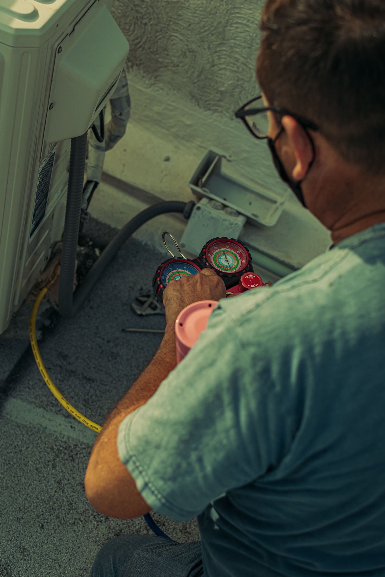 Technician using gauges beside an outdoor air-conditioning unit